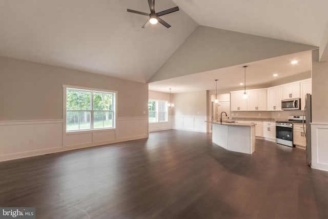 interior space featuring a kitchen island with sink, high vaulted ceiling, dark wood-type flooring, white cabinets, and stainless steel appliances