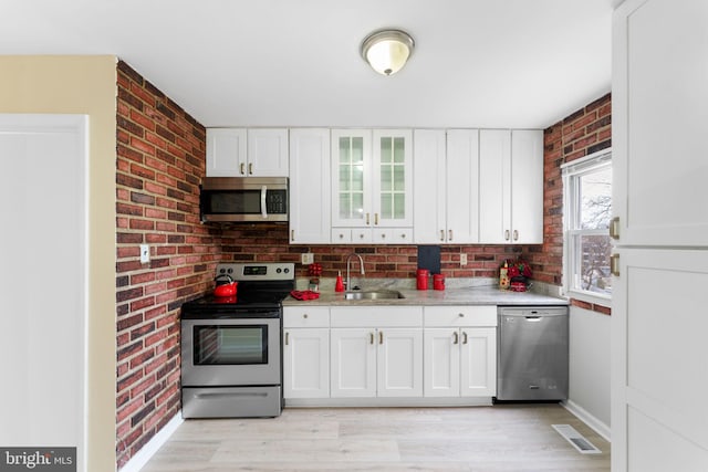 kitchen featuring white cabinets, sink, light hardwood / wood-style floors, stainless steel appliances, and brick wall