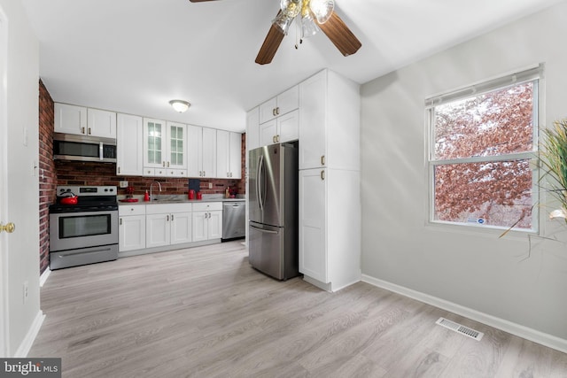 kitchen with white cabinets, decorative backsplash, light hardwood / wood-style floors, and stainless steel appliances