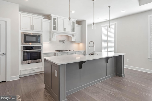 kitchen featuring stainless steel appliances, sink, white cabinetry, hanging light fixtures, and a kitchen island with sink