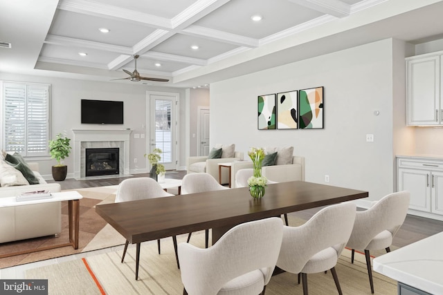 dining area with coffered ceiling, a premium fireplace, crown molding, ceiling fan, and beamed ceiling