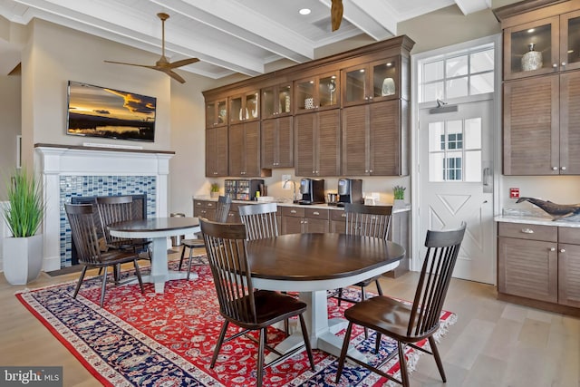 dining room with light hardwood / wood-style flooring, crown molding, a tiled fireplace, ceiling fan, and beamed ceiling