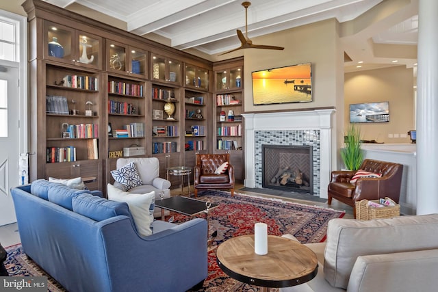 living room featuring a tile fireplace, beamed ceiling, ceiling fan, built in features, and crown molding