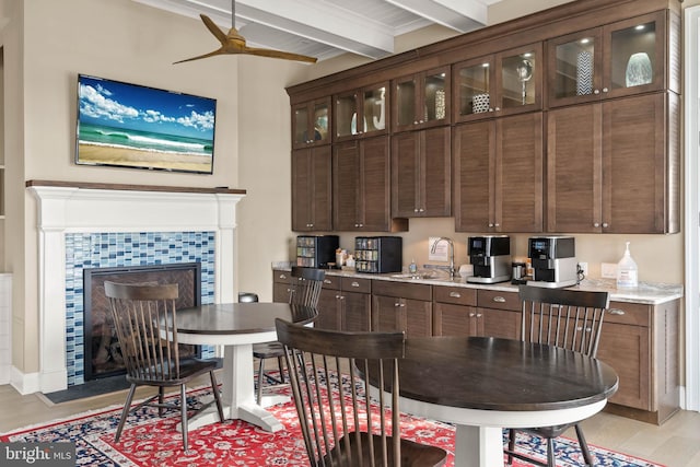 kitchen featuring a tiled fireplace, beam ceiling, dark brown cabinetry, and sink