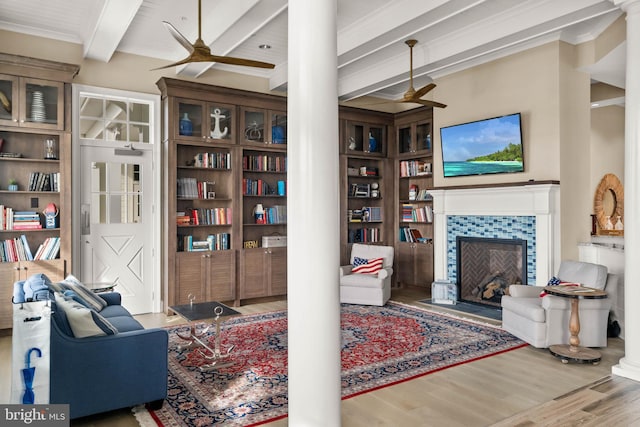 living room with a tile fireplace, beamed ceiling, ornamental molding, hardwood / wood-style flooring, and built in shelves