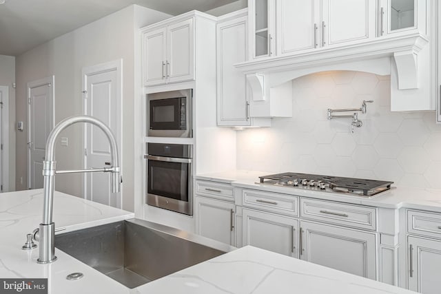 kitchen featuring appliances with stainless steel finishes, light stone countertops, sink, white cabinetry, and backsplash