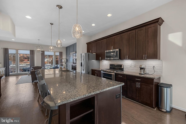 kitchen featuring decorative light fixtures, dark brown cabinetry, an island with sink, and appliances with stainless steel finishes