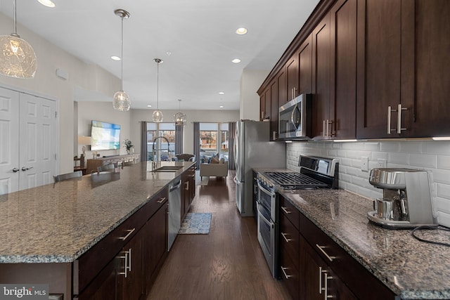 kitchen with backsplash, stainless steel appliances, dark stone countertops, hanging light fixtures, and a large island