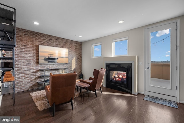 living area with a multi sided fireplace, dark wood-type flooring, and brick wall