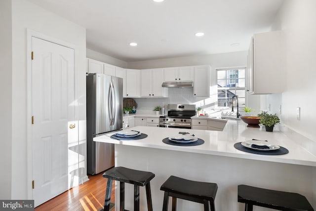 kitchen featuring appliances with stainless steel finishes, sink, white cabinets, a kitchen breakfast bar, and kitchen peninsula