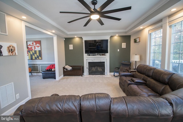 carpeted living room featuring ceiling fan, ornamental molding, a fireplace, and a tray ceiling