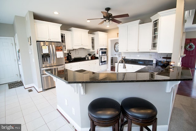 kitchen featuring backsplash, kitchen peninsula, a kitchen bar, white cabinets, and appliances with stainless steel finishes