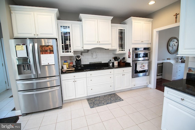 kitchen with light tile patterned floors, backsplash, dark stone counters, white cabinets, and appliances with stainless steel finishes