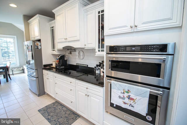 kitchen with decorative backsplash, appliances with stainless steel finishes, dark stone countertops, white cabinetry, and light tile patterned flooring