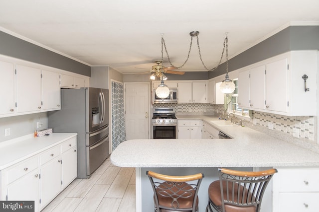 kitchen featuring appliances with stainless steel finishes, kitchen peninsula, hanging light fixtures, and white cabinets