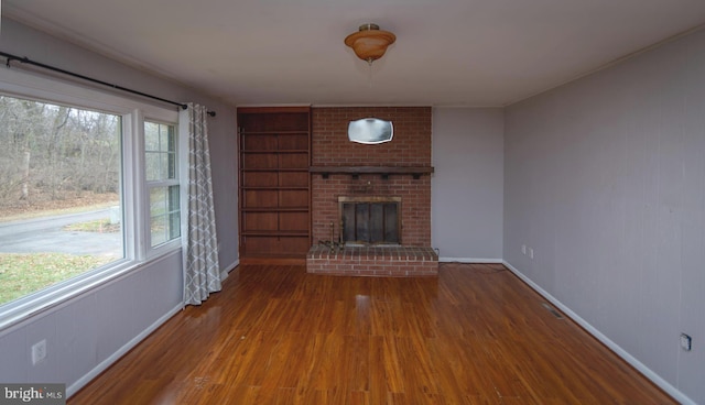 unfurnished living room with wood-type flooring and a brick fireplace