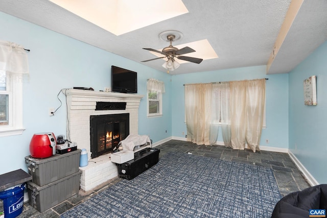 living room featuring ceiling fan, a healthy amount of sunlight, a textured ceiling, and a brick fireplace