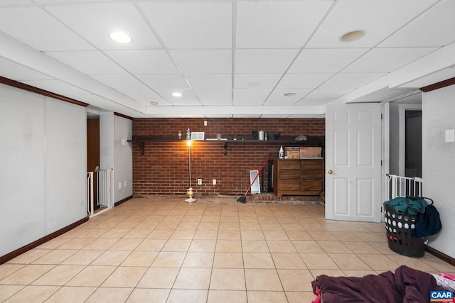 basement with a drop ceiling, light tile patterned flooring, and brick wall