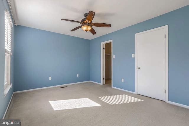 unfurnished bedroom with a walk in closet, light colored carpet, and ceiling fan