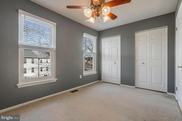 unfurnished bedroom featuring multiple closets, light colored carpet, and ceiling fan