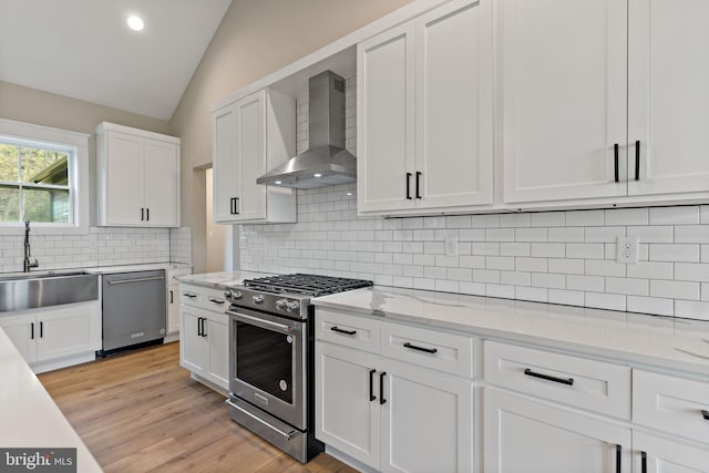 kitchen featuring sink, wall chimney exhaust hood, stainless steel appliances, backsplash, and lofted ceiling