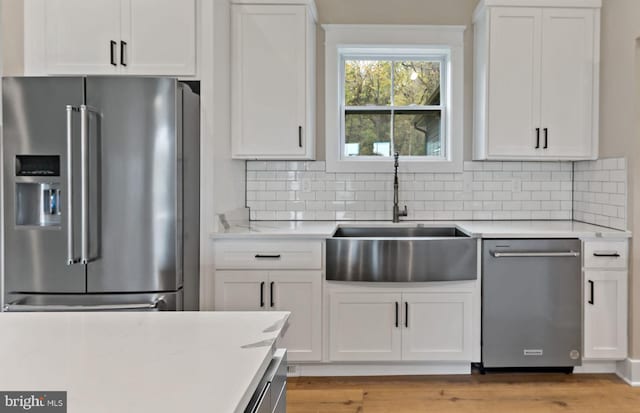 kitchen with backsplash, white cabinetry, light hardwood / wood-style flooring, and stainless steel appliances