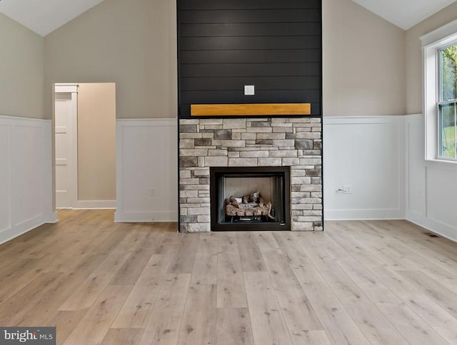 unfurnished living room with light hardwood / wood-style flooring, vaulted ceiling, and a stone fireplace