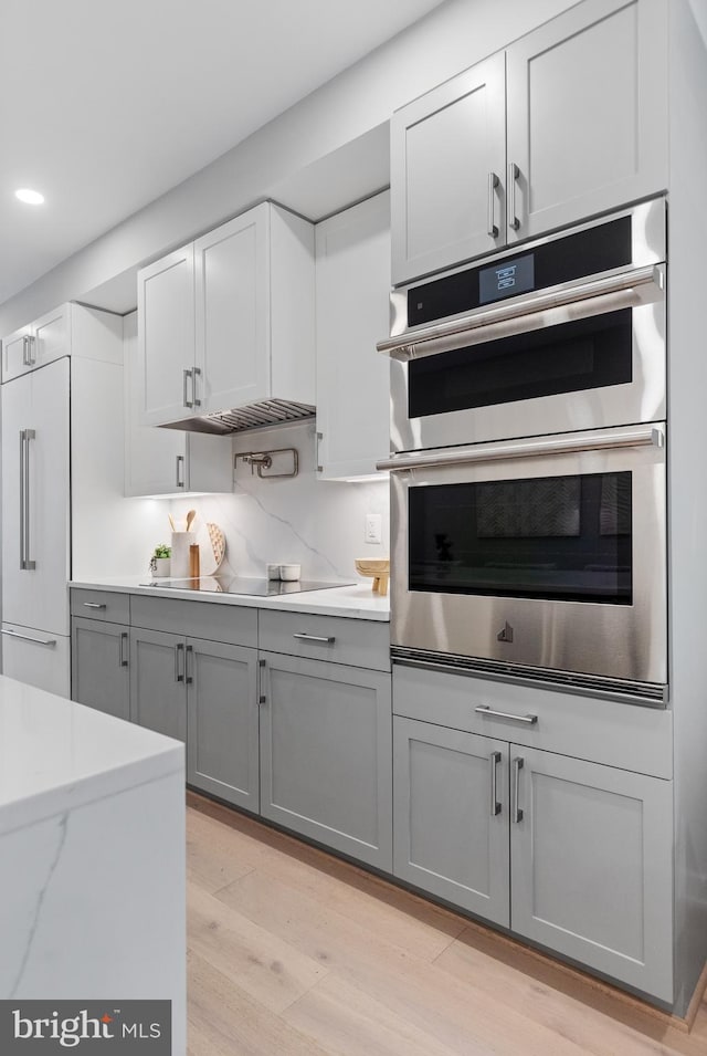 kitchen featuring cooktop, double oven, light hardwood / wood-style flooring, gray cabinets, and built in refrigerator