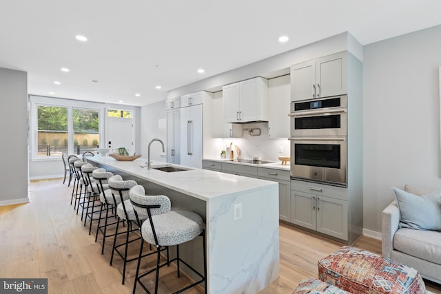 kitchen with light stone countertops, sink, stainless steel double oven, an island with sink, and electric stovetop