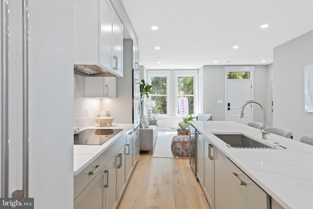 kitchen featuring light stone countertops, sink, light hardwood / wood-style flooring, and black electric stovetop