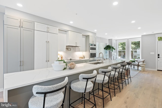 kitchen with a large island with sink, light wood-type flooring, a breakfast bar area, and sink