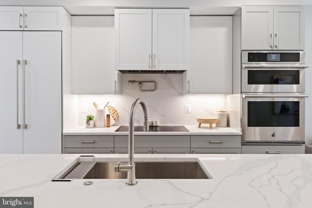 kitchen featuring light stone countertops, double oven, sink, white cabinets, and built in refrigerator