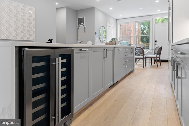 kitchen featuring light wood-type flooring, beverage cooler, gray cabinetry, and an island with sink