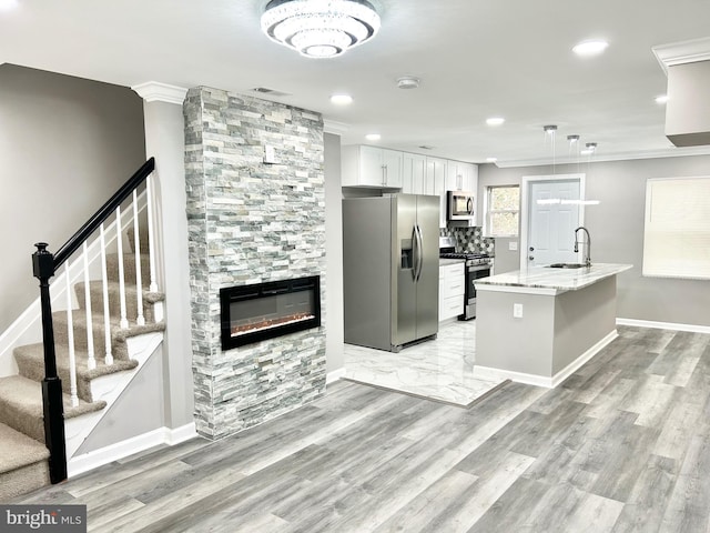 kitchen with white cabinetry, sink, a stone fireplace, a kitchen island with sink, and appliances with stainless steel finishes