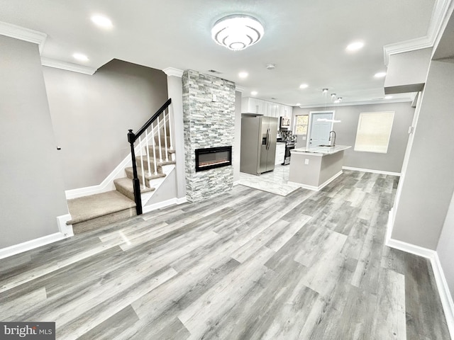 unfurnished living room featuring crown molding, light hardwood / wood-style floors, a stone fireplace, and sink