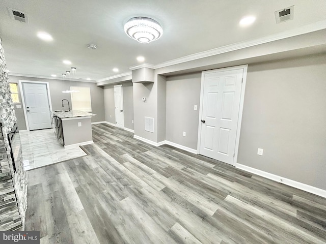 basement with light wood-type flooring, ornamental molding, and sink