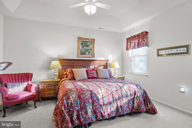 bedroom with light carpet, ceiling fan, and a tray ceiling