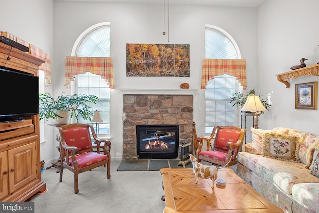 carpeted living room featuring a high ceiling and a stone fireplace