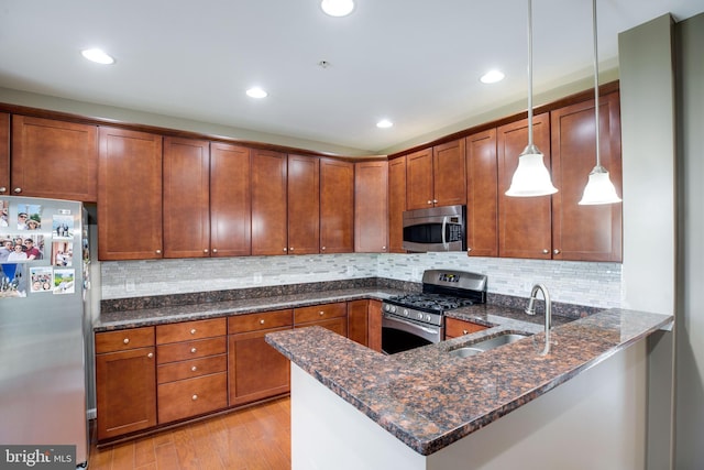 kitchen with kitchen peninsula, stainless steel appliances, decorative light fixtures, dark stone countertops, and light hardwood / wood-style floors