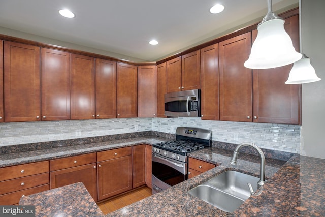 kitchen with light wood-type flooring, stainless steel appliances, sink, pendant lighting, and dark stone countertops