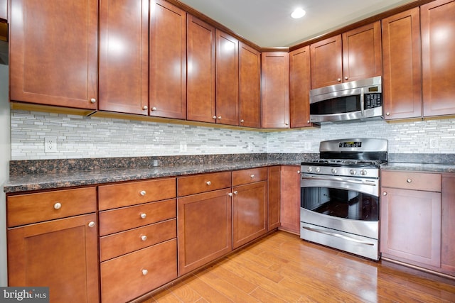 kitchen with backsplash, dark stone counters, stainless steel appliances, and light hardwood / wood-style floors