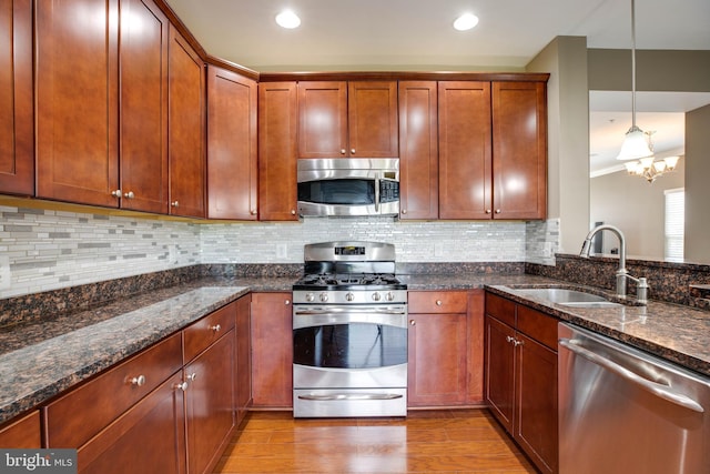 kitchen featuring dark stone counters, sink, appliances with stainless steel finishes, decorative light fixtures, and light hardwood / wood-style floors