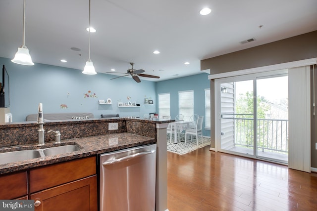 kitchen with stainless steel dishwasher, sink, wood-type flooring, dark stone countertops, and hanging light fixtures