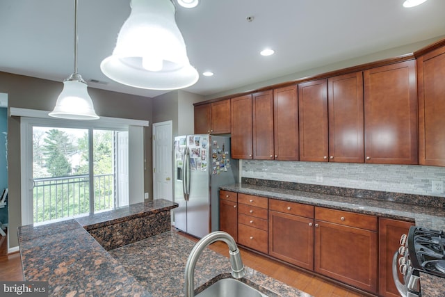 kitchen with pendant lighting, dark stone counters, light wood-type flooring, tasteful backsplash, and stainless steel appliances