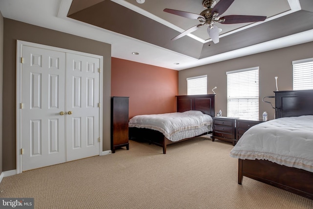 bedroom with ceiling fan, a raised ceiling, and light carpet