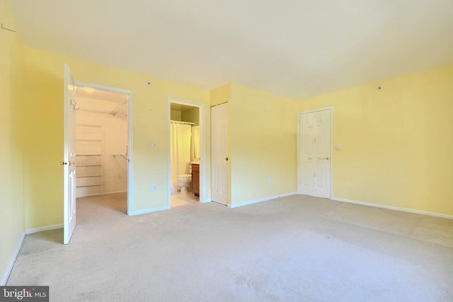 unfurnished bedroom featuring ensuite bathroom, light carpet, and a spacious closet