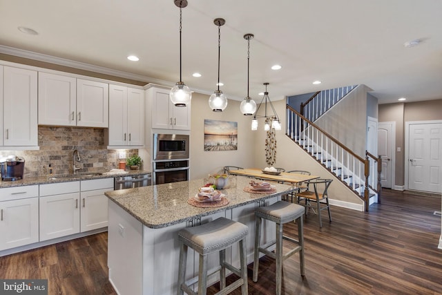 kitchen with sink, hanging light fixtures, a kitchen island, white cabinetry, and stainless steel appliances