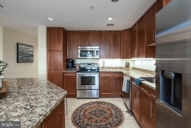 kitchen featuring light tile patterned floors, stainless steel appliances, light stone counters, and sink