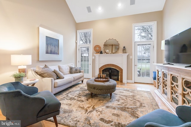 living room featuring light wood-type flooring, high vaulted ceiling, and a tiled fireplace