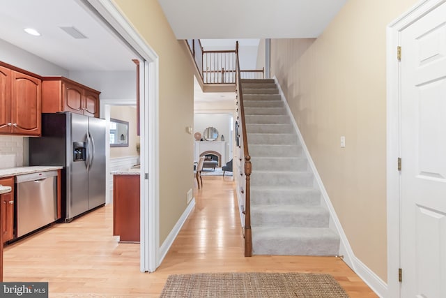 kitchen featuring light stone counters, tasteful backsplash, stainless steel appliances, and light hardwood / wood-style flooring